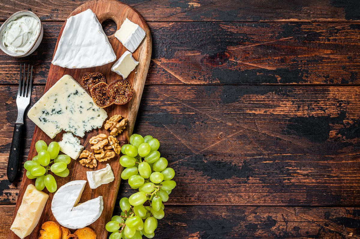 Cheeseboard with a variety of cheeses, grapes and walnuts on a dark wooden table