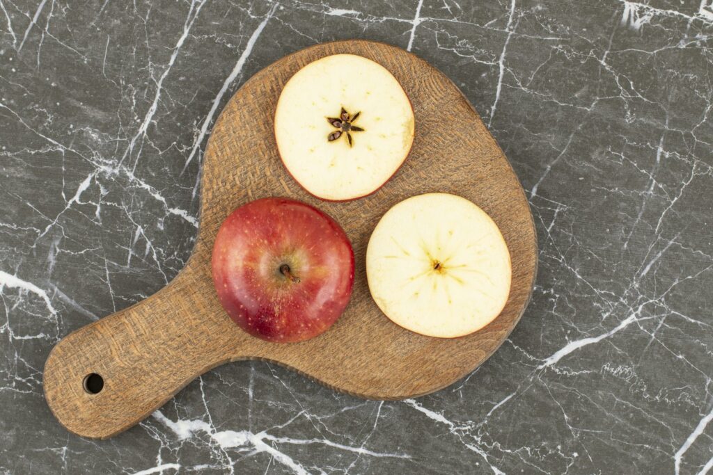 Whole and quartered red apple on a wooden board
