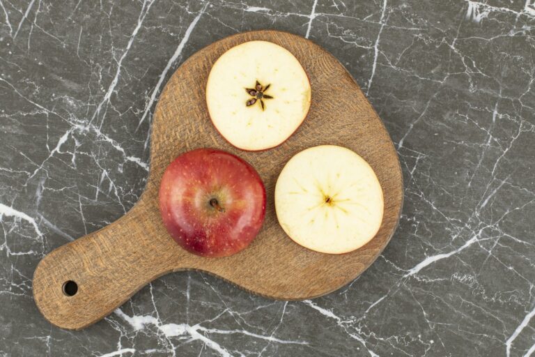 Whole and quartered red apple on a wooden board