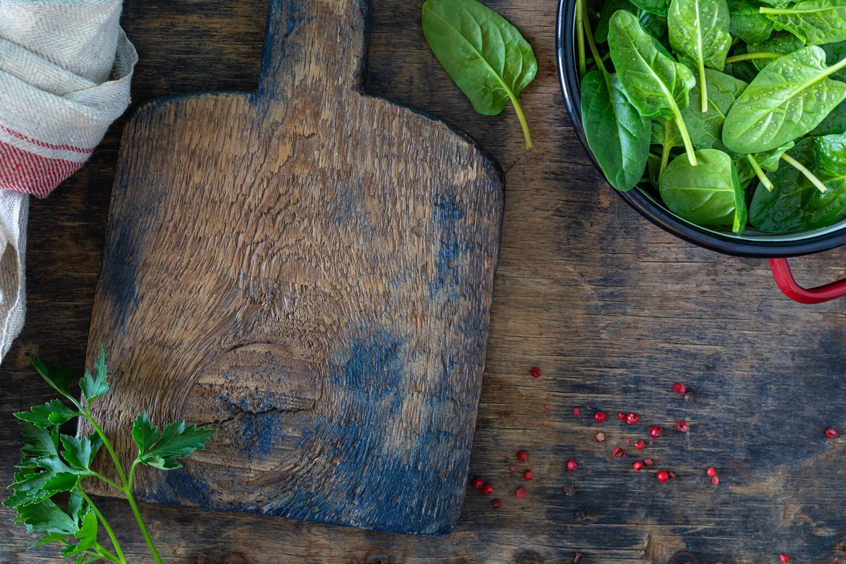 Fresh spinach leaves in a bowl next to a wooden board