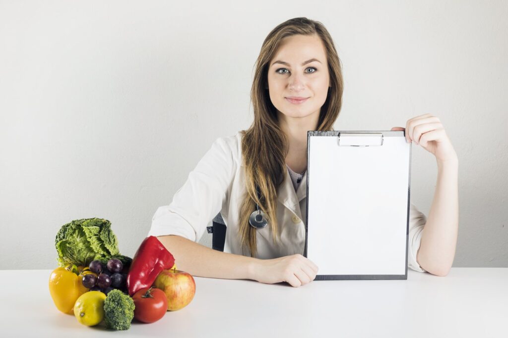 Nutrition professional in a white coat holding a clipboard, next to fruit and vegetables
