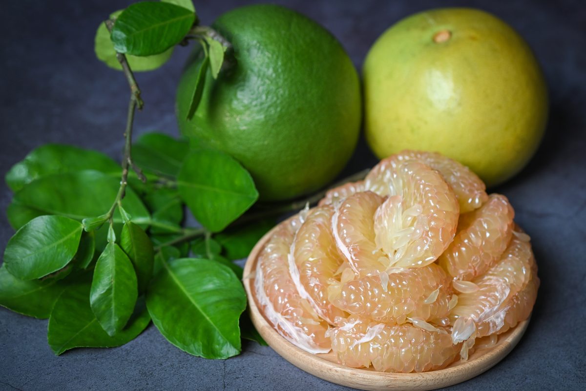 Pomelo segments on a wooden plate next to whole fruit