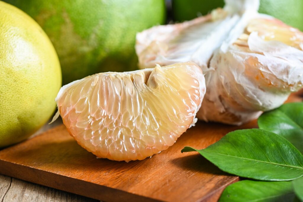 Peeled pomelo segments on a wooden board with leaves