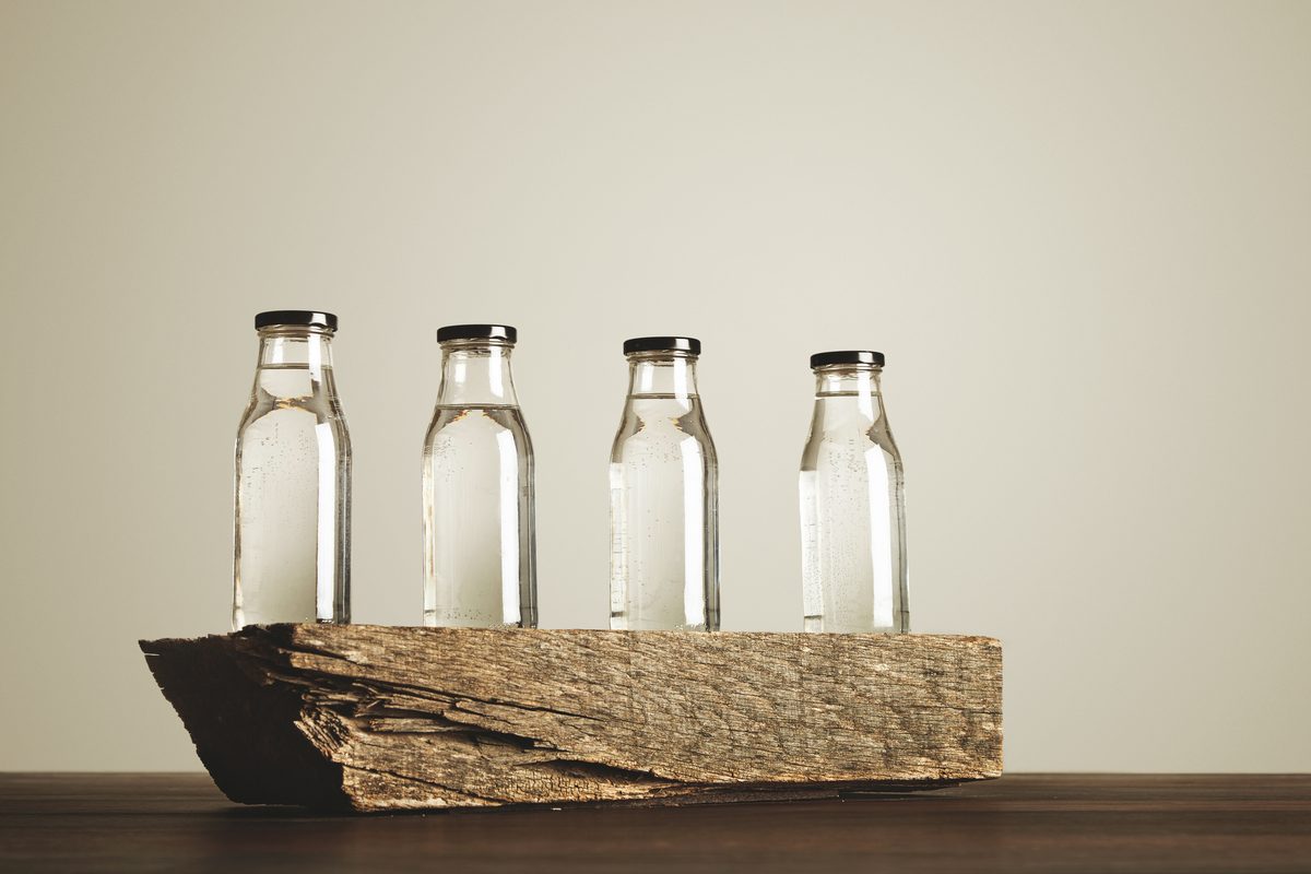 Quatre bouteilles d'eau en verre posées sur une bûche