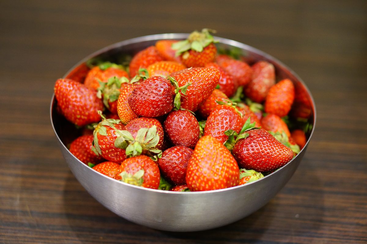 Stainless steel bowl filled with fresh strawberries on a wooden table