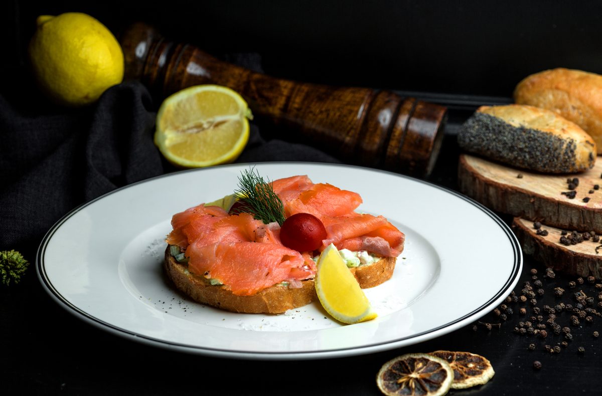 Open sandwich of smoked salmon and avocado served with a lemon wedge