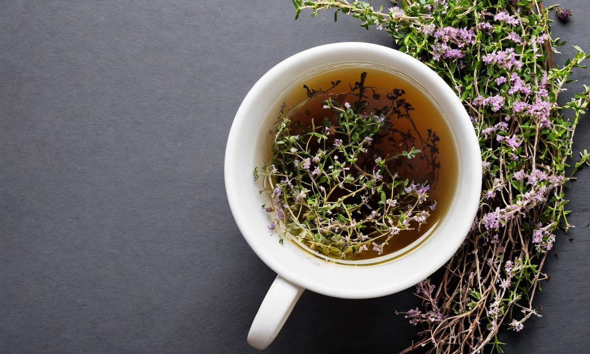 White cup of thyme tea with sprigs of flowering thyme