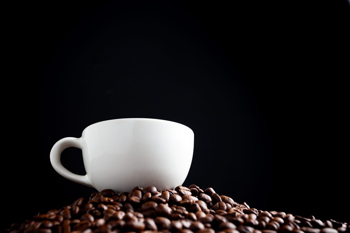 Tasse blanche posée sur un tas de grains de café torréfiés