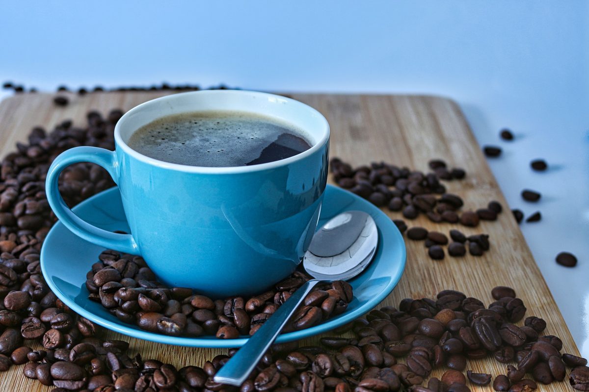 Blue cup of black coffee surrounded by coffee beans