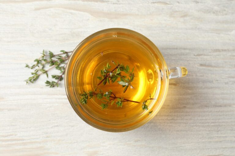 Cup of fresh thyme infusion on a wooden table seen from above