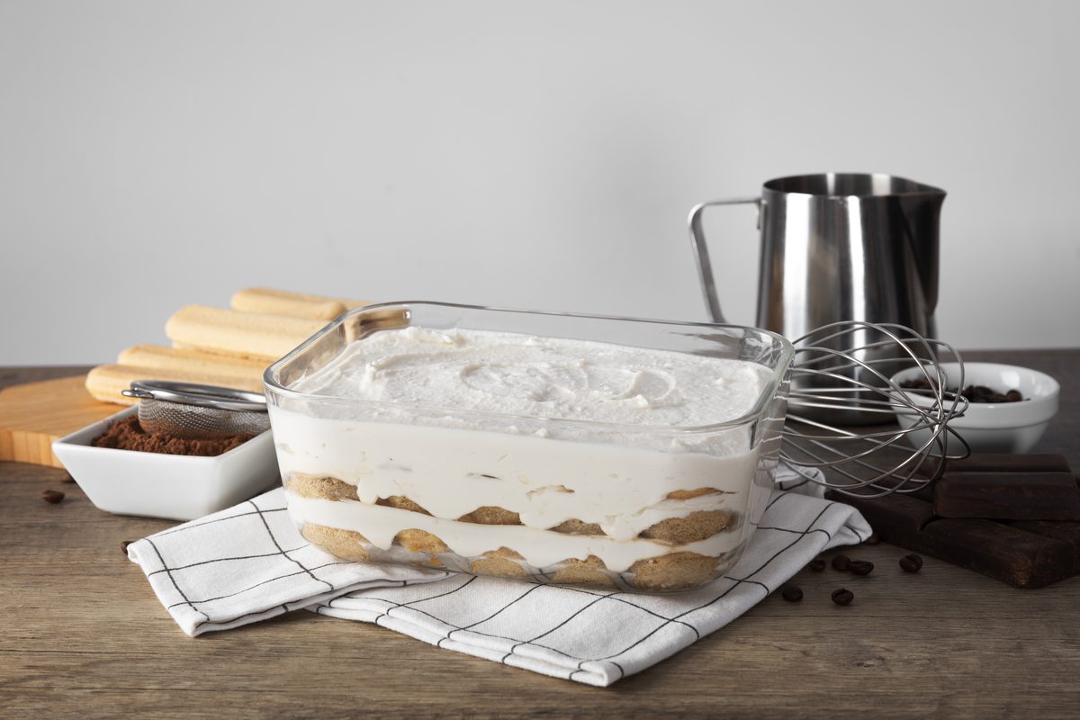 Homemade tiramisu being assembled in a glass dish with sponge fingers
