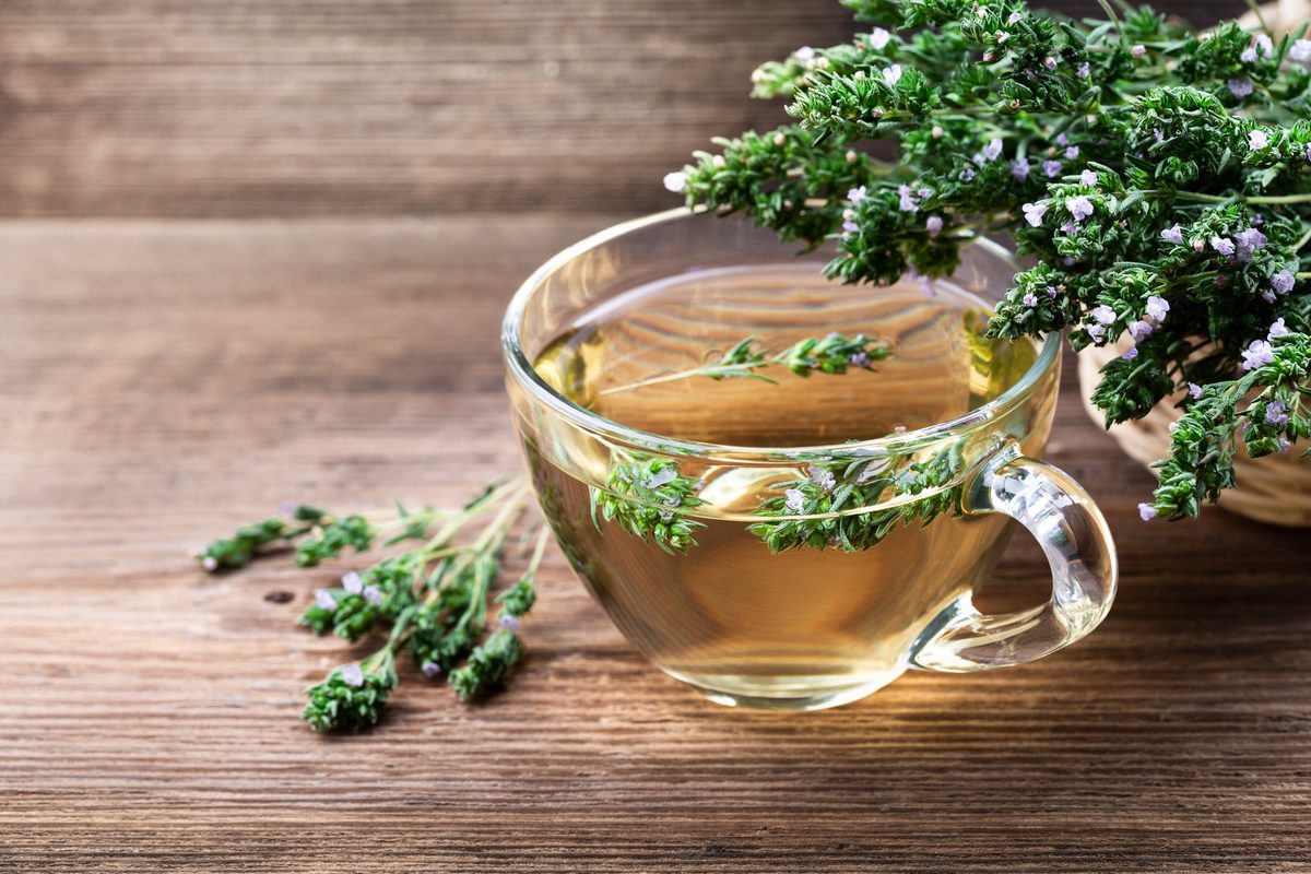 Thyme tea in a glass cup, sprigs of flowering thyme on wood