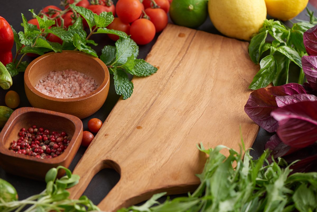 Tomatoes, lemons, fresh herbs and spices around a wooden board