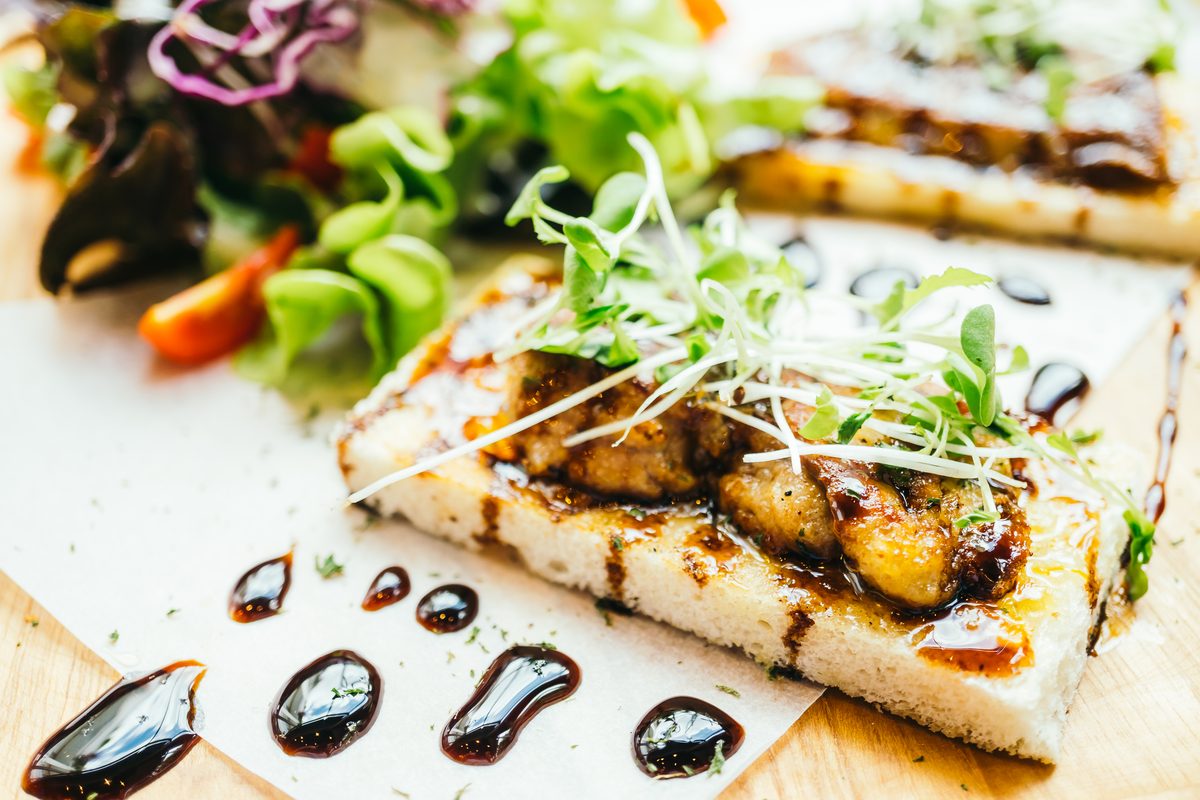 Slice of pan-fried foie gras on toasted bread with shoots and balsamic reduction
