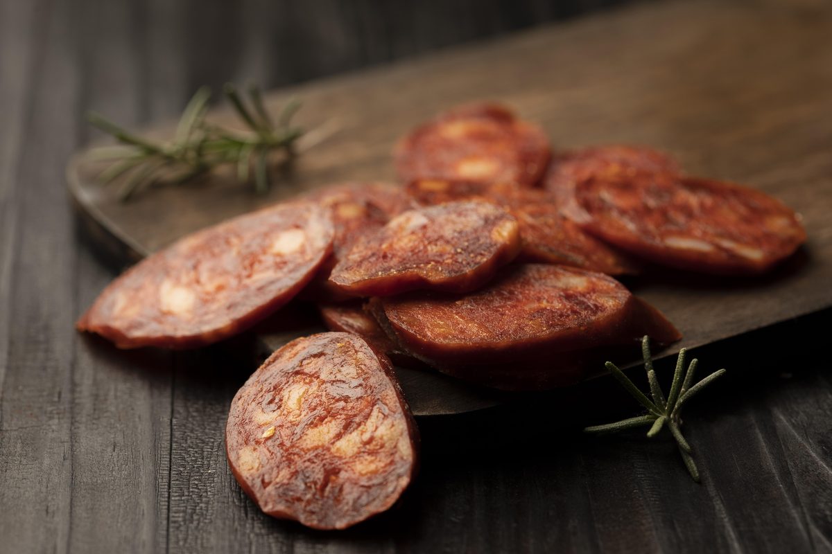 Slices of dry chorizo on a wooden board with rosemary