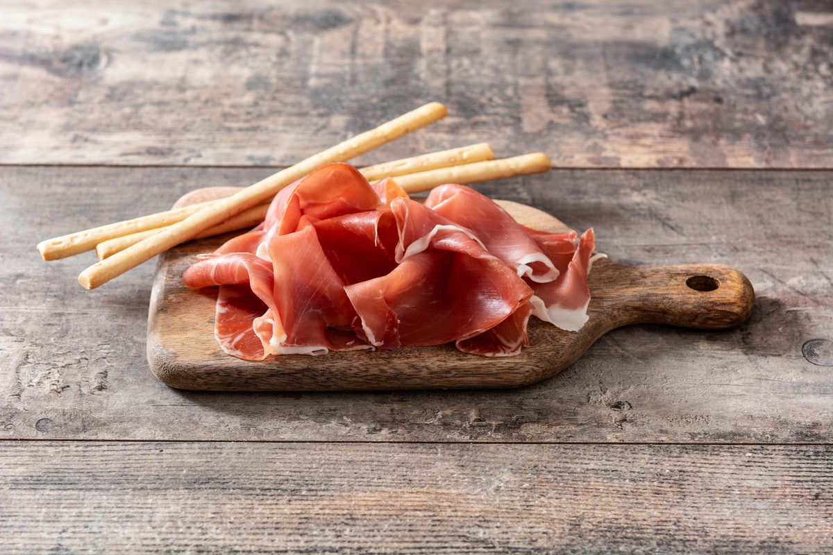 Slices of serrano ham and breadsticks on a wooden board