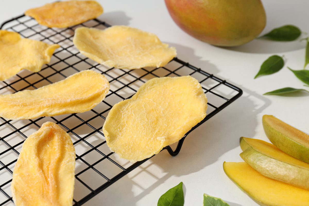Slices of dried mango on a rack next to a fresh mango