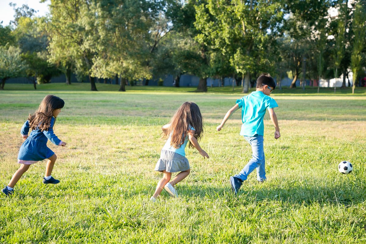 Three children playing with a ball on the lawn of a park