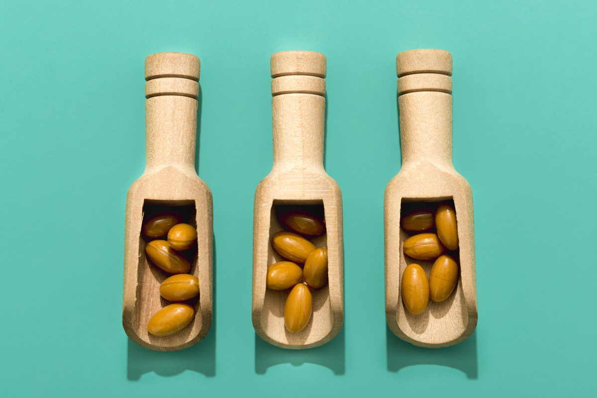 Three wooden scoops filled with orange capsules on a turquoise background