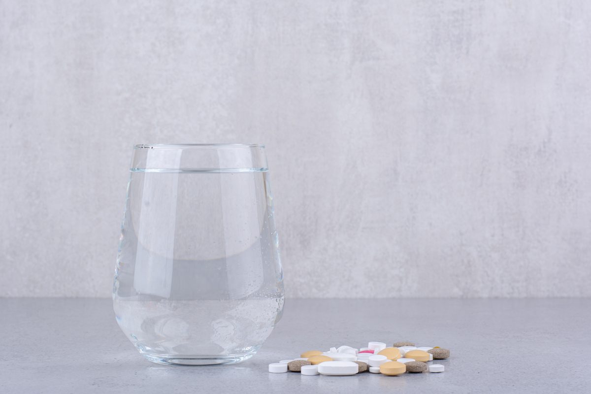 Glass of water and tablets of various colours on a grey table