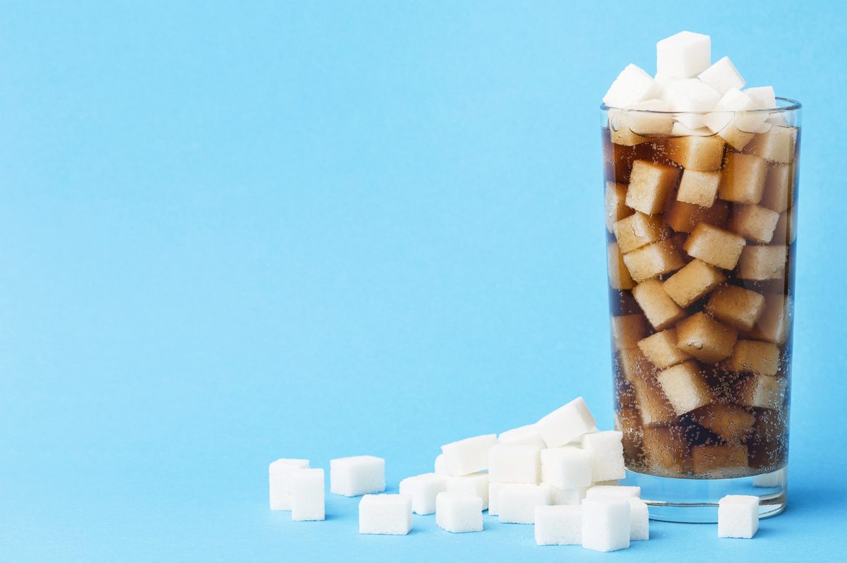 Glass of soda filled with sugar cubes on a blue background