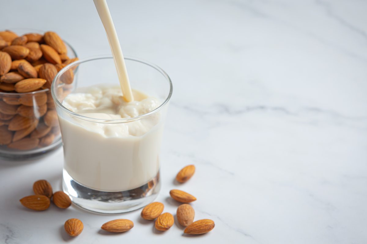 Almond drink poured into a glass next to a bowl of almonds