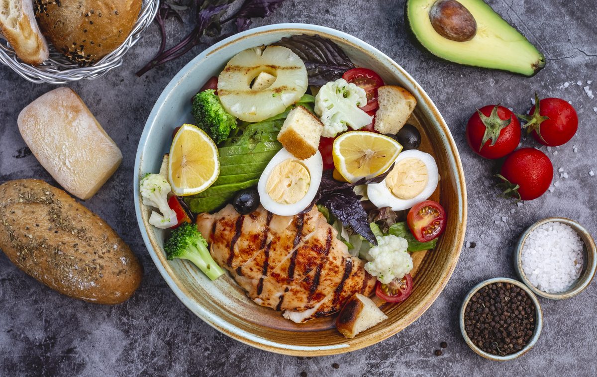 Complete bowl of grilled chicken, hard-boiled egg, broccoli, cauliflower, avocado and raw vegetables