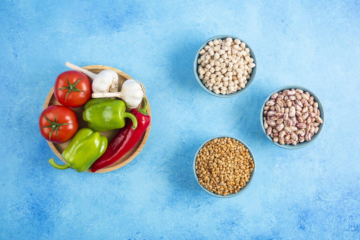 Bowls of chickpeas, beans and lentils next to fresh vegetables