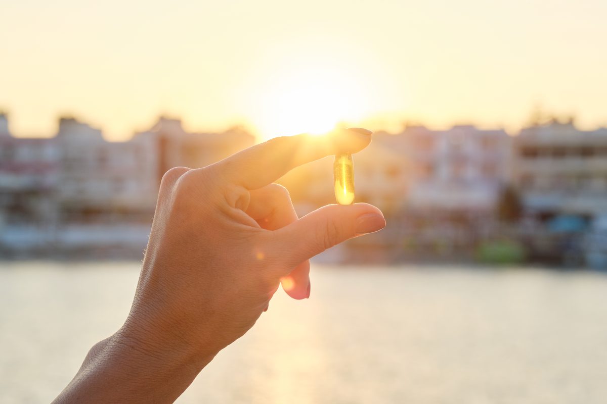 Vitamin D capsule held between two fingers facing the setting sun