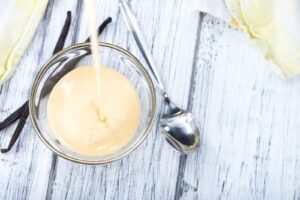 Crème anglaise versée dans un bol en verre près de gousses de vanille
