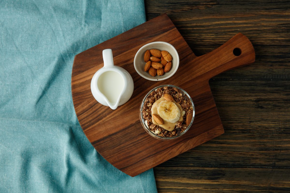 Banana granola, a small jug of milk and almonds on a wooden board