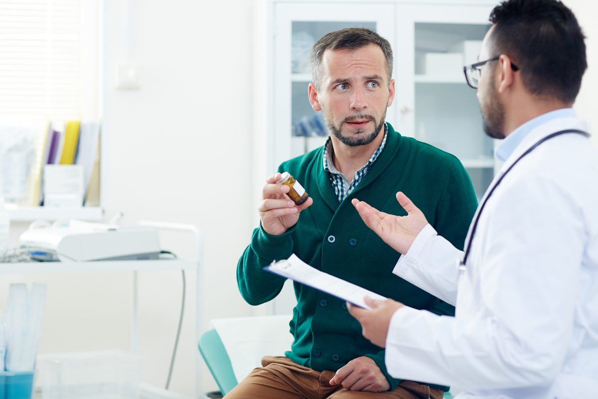 Man consulting a doctor and holding a bottle of medicine