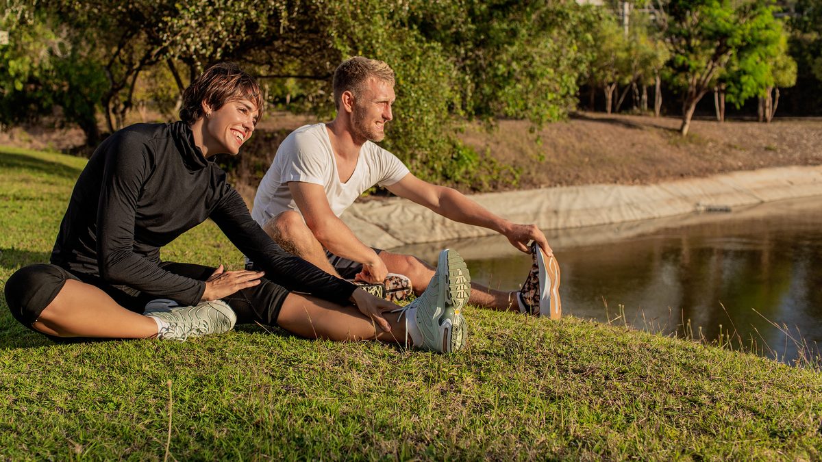Homme et femme s'étirant sur l'herbe d'un parc avant leur course