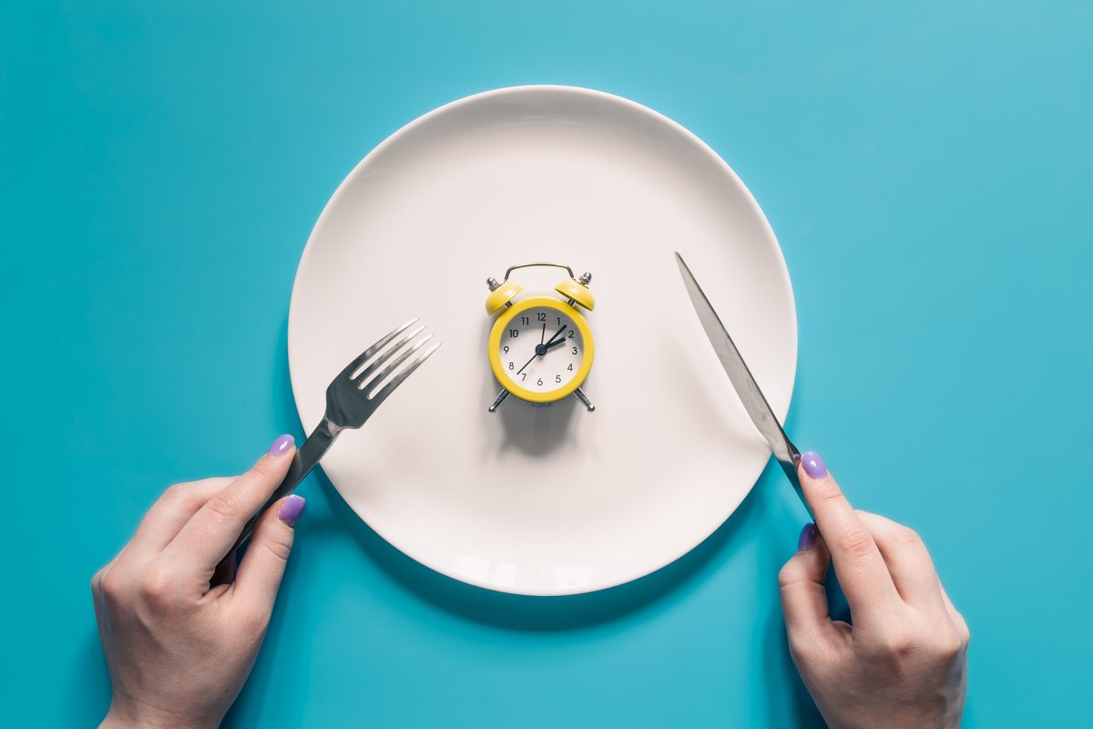 Hands holding a knife and fork around a plate containing a small alarm clock