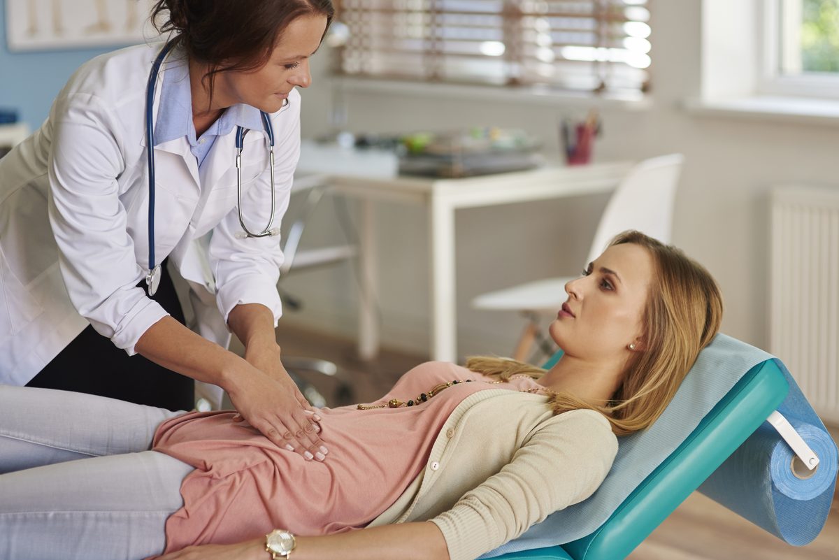 Médecin palpant le ventre d'une patiente allongée sur une table d'examen
