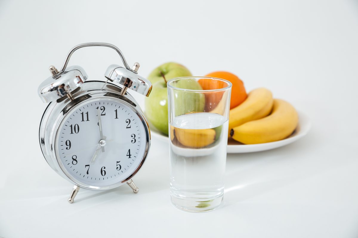 Alarm clock, glass of water and plate of fruit on a white table