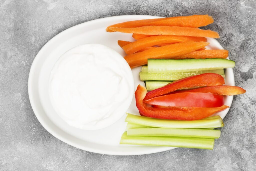 White sauce in an oval dish with carrot, pepper and cucumber sticks
