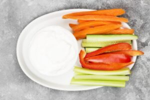 Sauce blanche dans un plat ovale avec bâtonnets de carotte, de poivron et de concombre