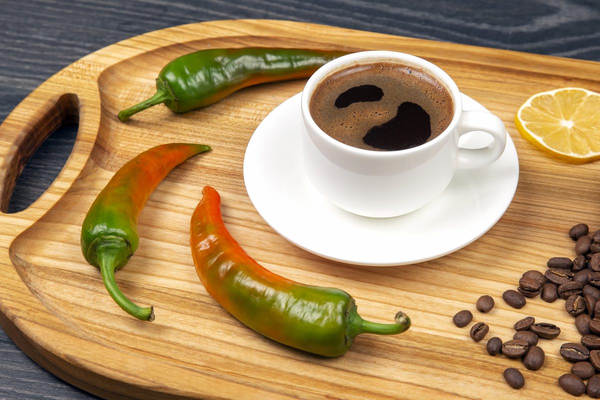 Cup of black coffee surrounded by chilli peppers and a slice of lemon