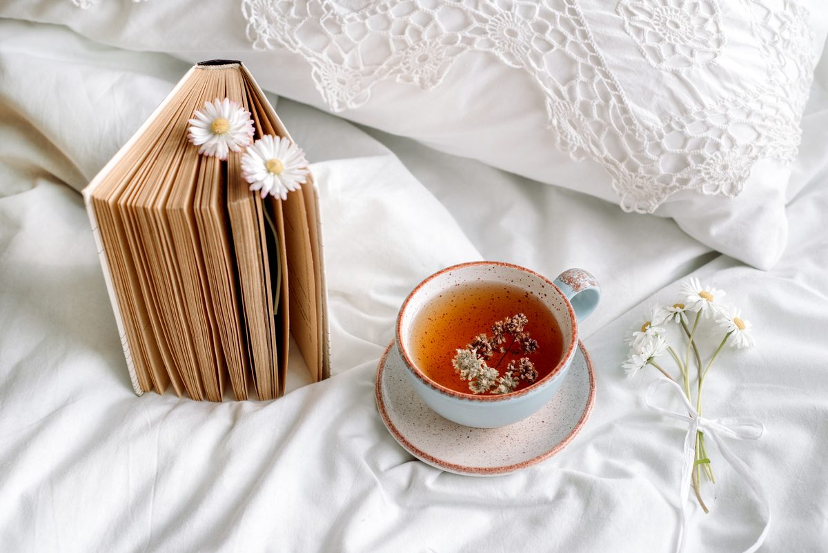 Cup of chamomile tea resting on a bed next to a book