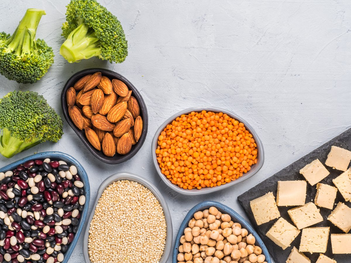 Tofu, red lentils, quinoa, chickpeas, beans, almonds and broccoli on a grey background