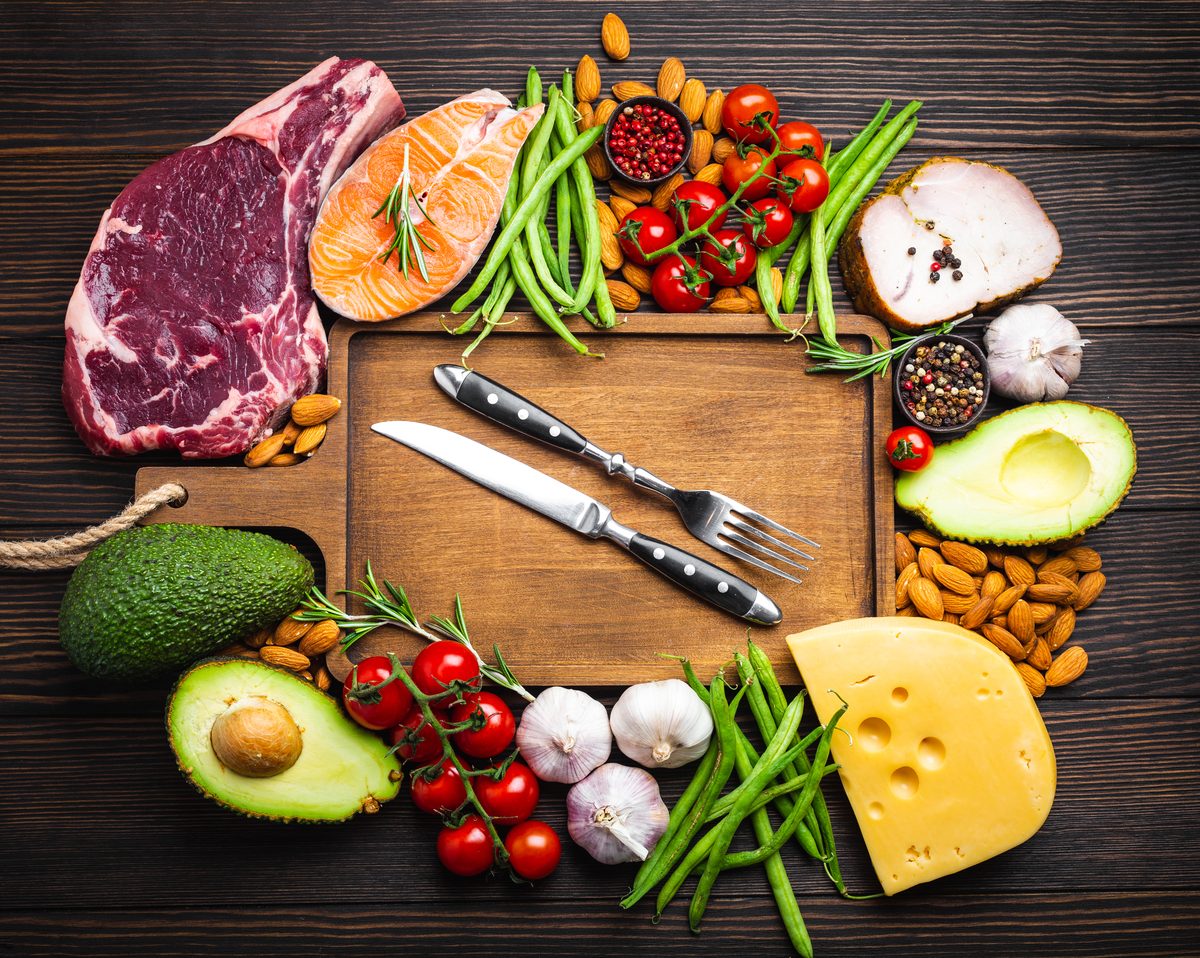 Red meat, salmon, avocado, cheese, green beans and almonds around a board